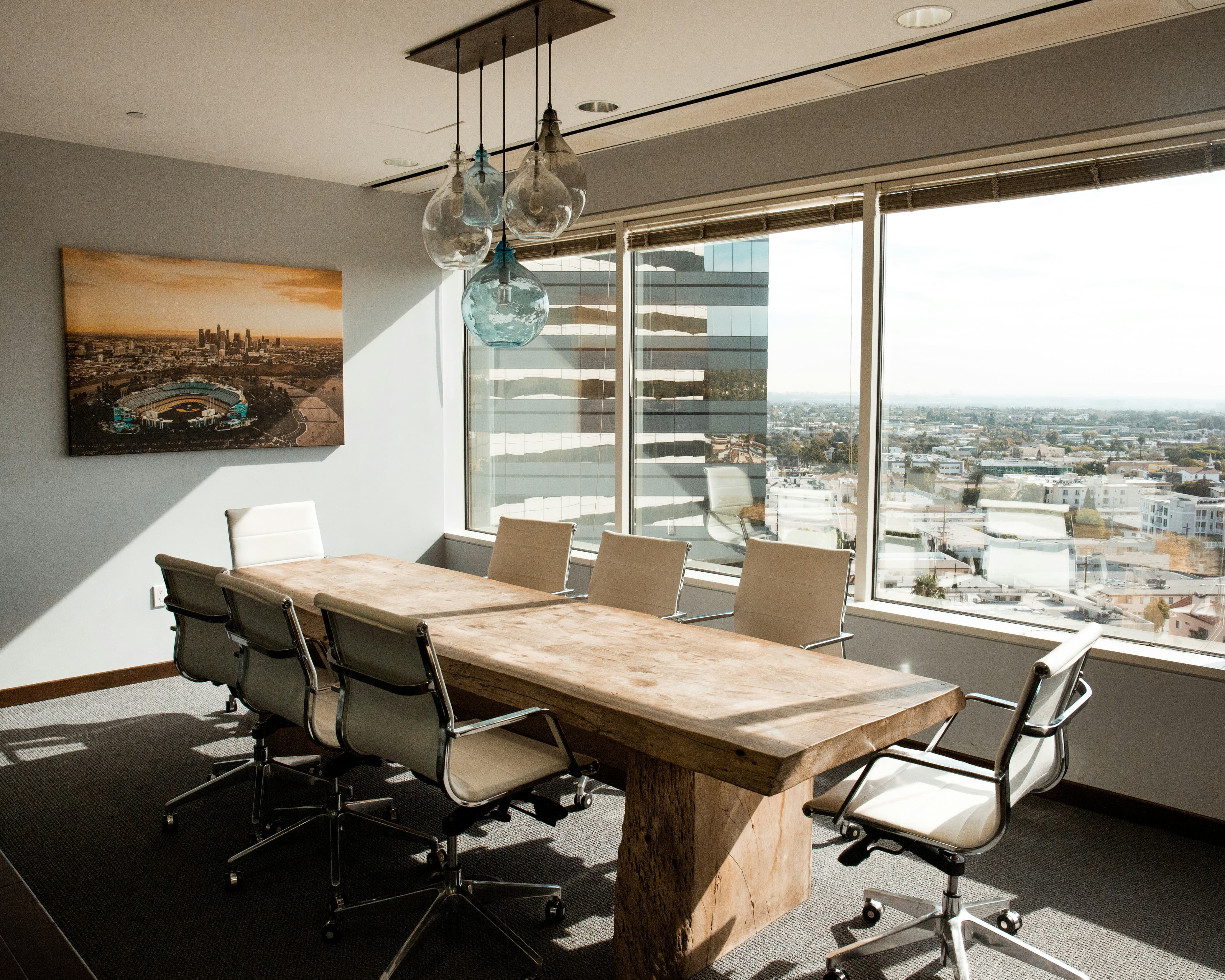 Sala de reuniones con mesa de madera, sillas blancas y luz natural