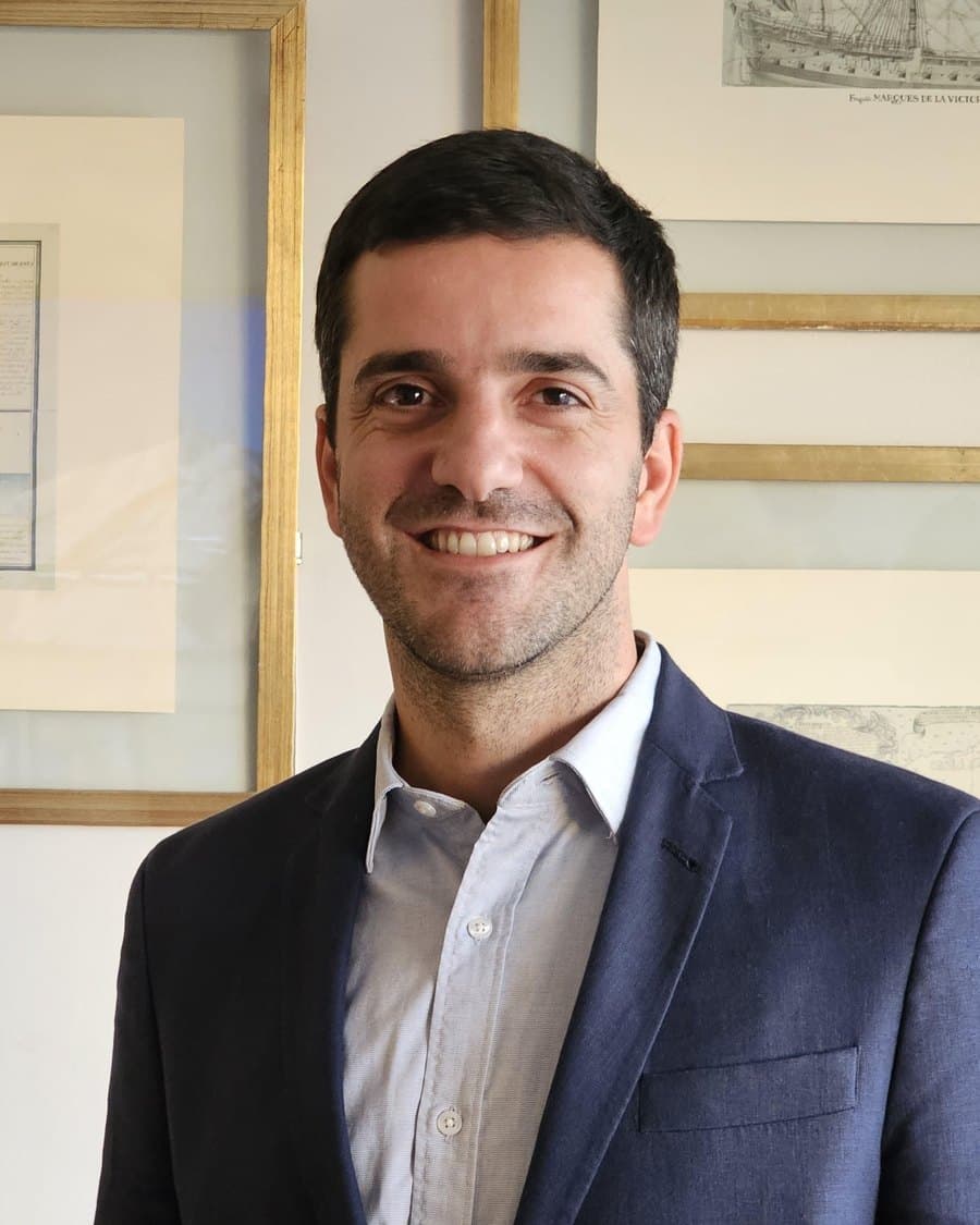 Mateo Gourdy Allende, de saco azul, frente a grabados náuticos enmarcados
